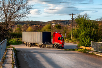 Red truck with grey cargo container maneuvering on a crossroads at setting sun light