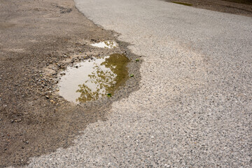 Water reflecting trees in pothole on damaged asphalt road