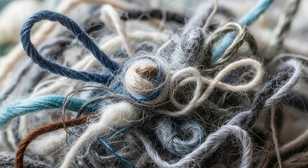 A tangled close-up of a messy pile of thick, soft, and textured yarn and wool in various shades of grey, white, and blue.