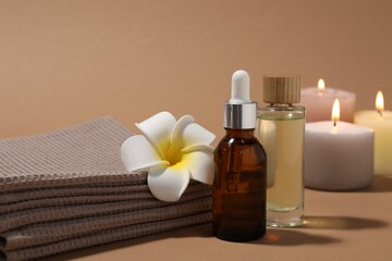 Folded waffle towels, bottles of cosmetic products and plumeria flower on light brown background, closeup