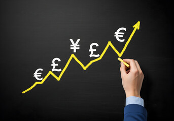 Hand drawing an upward trend line with various currency symbols on a chalkboard. Represents global finance, currency growth, and economic trends.