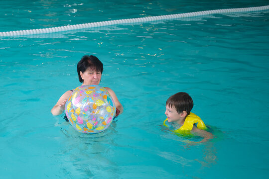 Woman coaching a boy to swim in an indoor pool with a colorful beach ball. Learning to swim and water safety concept. A child aged four years.