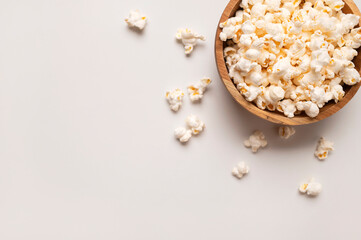 White salty or sweet popcorn in wooden bowl on light gray background, top view flat lay. Corn flakes, food for movie or cinema. Delicious appetizer, party snack. Empty space for text