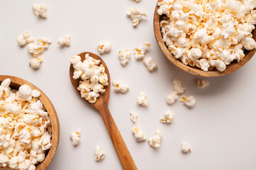 White salty or sweet popcorn in wooden bowl and a spoon on light gray background, top view flat lay. Corn flakes, food for movie or cinema. Delicious appetizer, party snack. Empty space for text