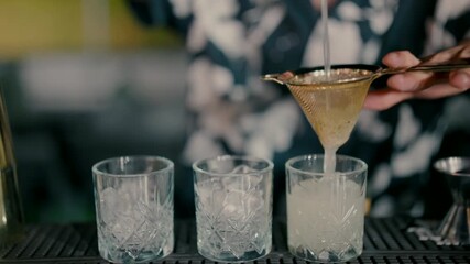Professional bartender making an alcoholic cocktail' pouring drink through strainer into glass. Close-up mixology and nightlife concept.