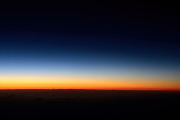Obraz premium Aerial view of a twilight horizon. Colors blend from dark blue to orange-red at the horizon line, above a dark expanse of clouds