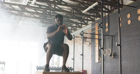 African American male using mental prep before leaping onto plyometric box in gym for power - Powered by Adobe