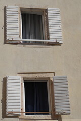 Fototapeta premium Two old windows with open white wooden shutters on a yellow plastered wall, a detail of traditional European architecture