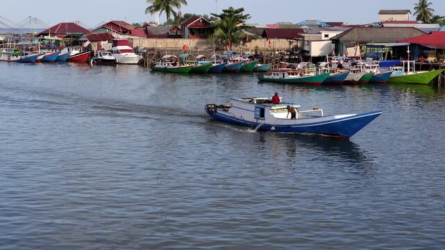 Traditional fishing activities using wooden boats on the Manggar River with a background of a row of boats anchored in the fishing village in the afternoon