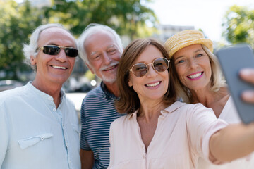 Happy group of mature friends smiling and taking a selfie outdoors on a sunny day