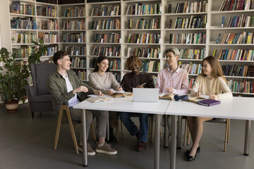 Sharing knowledge and peer learning. Happy international group diverse teenage students gather at library work on joint scientific project study academic materials together using books web resources