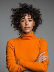 Studio portrait of a young happy afro woman looking to the camera, light grey background, wearing an orange turtle neck