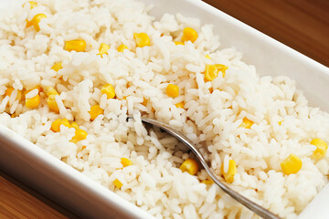 Cooked white rice with corn. Closeup view of warm steamed rice mixed with yellow sweet corn. Served in white ceramic dish with spoon. Homemade vegetarian meal. Healthy and simple food background.