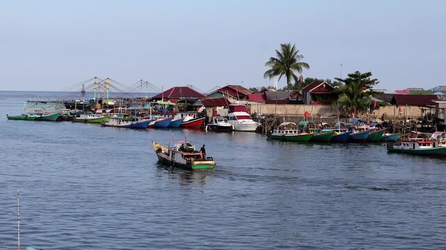 Traditional fishing activities using wooden boats on the Manggar River with a background of a row of boats anchored in the fishing village in the afternoon
