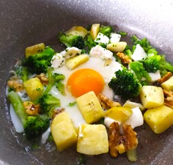 Fried eggs with broccoli, potatoes and walnuts in a pan, close-up, isolated, vegetarian breakfast, cooking, healthy eating.