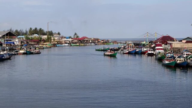 Traditional fishing activities using wooden boats on the Manggar River with a background of a row of boats anchored in the fishing village in the afternoon