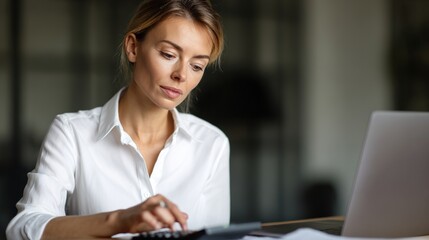 Focused Professional in Office: A focused woman, engrossed in her work, meticulously utilizes a calculator alongside a modern laptop in a bright, modern office environment.