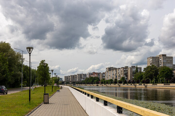 Urban river promenade with residential buildings, cloudy sky and streetlights before summer storm