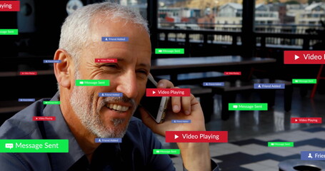 Man in polo shirt calling on smartphone, smiling at rooftop cafe table with floating digital labels
