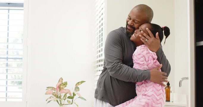 African American father and daughter greeting, hugging, making silly faces for fun at bathroom sink
