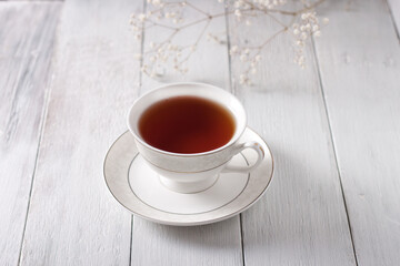 Aromatic hot tea in a white mug with a saucer rests on a white wooden table, bathed in natural morning light, creating cozy tranquility