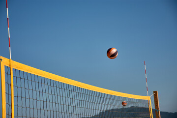 Volleyball in the air over a yellow net during a beach match in Baiona under a clear blue sky
