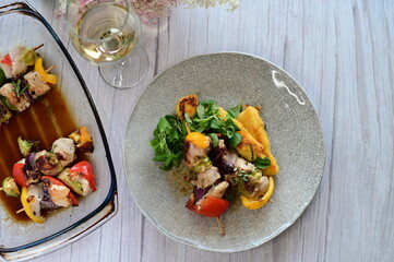 Top-down view of a colorful plated meal featuring a grilled chicken skewer, fresh salad, and creamy polenta on a white background.