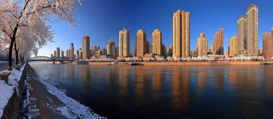 Obraz premium Cityscape reflected in a frozen river on a sunny winter day.