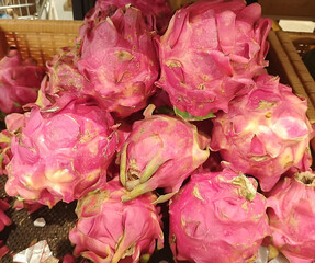 A vibrant pile of fresh exotic pink dragon fruits, also known as pitaya, displayed for sale in a market basket