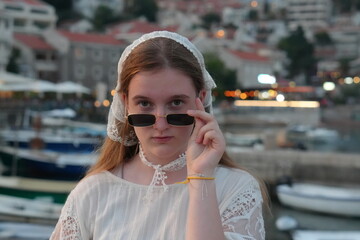 Stylish young woman with a lace headscarf and a choker, looking over her sunglasses at the camera with a serious expression