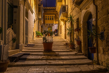 Charming narrow street in Birgu lit by warm evening lights, Malta.