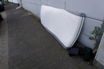 Old mattress and worn boots left on sidewalk outdoors