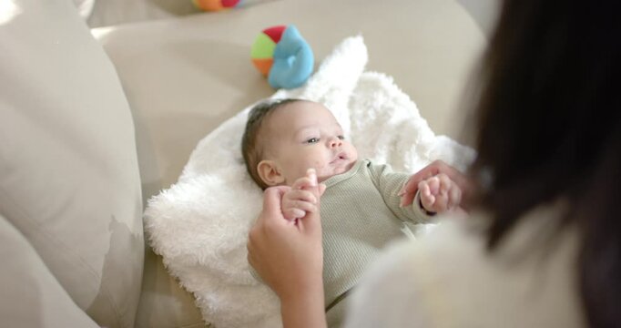 Female caregiver placing infant girl on cushion and guiding arms up and down for grip strength