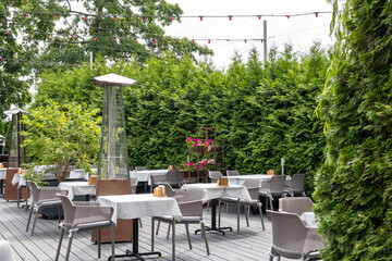 Outdoor restaurant terrace with tables, chairs, patio heaters and greenery in summer garden setting