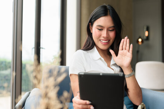 Young Asian woman in polo shirt using tablet computer indoors in hotel lounge or cafe - Powered by Adobe