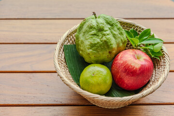top view photograph of small basket of fruit included with apple orange and guava on the wood table in sunshine