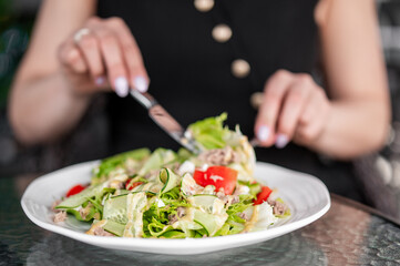 Close-up of a person eating fresh vegetable salad with tuna using fork and knife. Healthy meal on plate, featuring lettuce, cucumber, tomato, and creamy dressing.