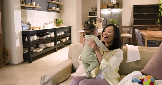 African American mother cradling infant, noticing ball, bouncing it to engage baby in living room