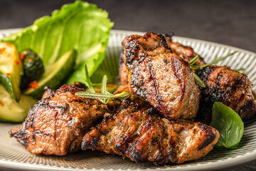 Grilled marinated pork pieces served with fresh greens and roasted zucchini on a ceramic plate