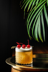 Elegant whiskey sour cocktail with foam and maraschino cherries on a golden tray. copy space