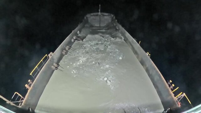 Hopper dredging ship seen from stern as it releases sediment in open sea during night ocean conditions