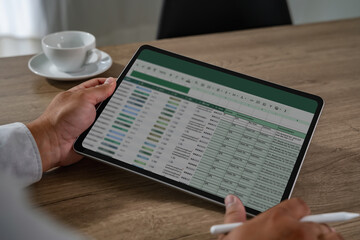 Spreadsheets to present finance data,person working spreadsheet tablet device sitting wooden table with cup of coffee nearby modern office setting