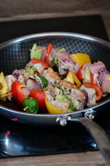 Homemade cooking with a frying pan filled with grilled skewers.