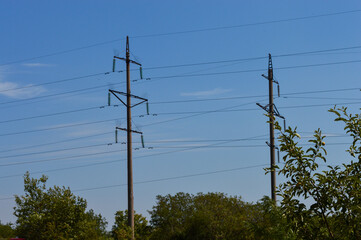 Obraz premium Electricity poles with overhead power lines against a clear blue sky and tree leaves in foreground.