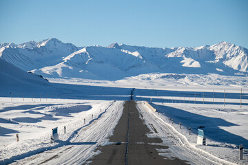 A straight asphalt road covered in snow and ice, leading towards a panoramic view of the snowcapped...