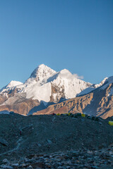 Fototapeta premium A line of tents on a rocky ridge with a breathtaking view of majestic snowcapped mountains in the background under a clear blue sky