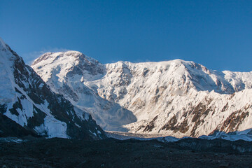 Fototapeta premium A wide shot of a majestic snow-covered mountain range with a large glacier flowing down the valley under a clear blue sky