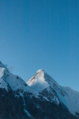 A snowcapped mountain peak stands out against a clear, dark blue starry night sky in a cold mountain landscape
