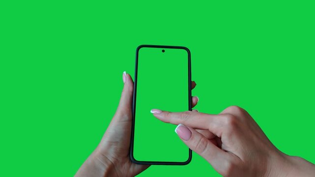 Young woman hand touch smartphone with green screen on green background. Phone in a female hand. Scrolling and swiping on a green phone screen. Template for scrolling through a feed in social network