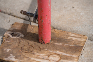 Support post anchored to wooden base on pavement for construction project in urban area during daylight hours